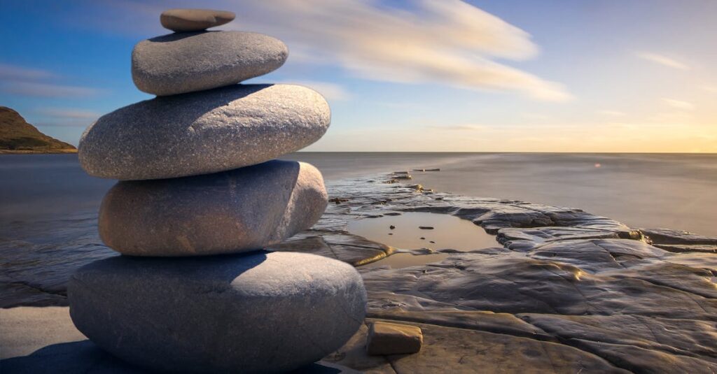A serene stack of stones on the rocky seashore during a peaceful sunrise, embodying balance and zen.